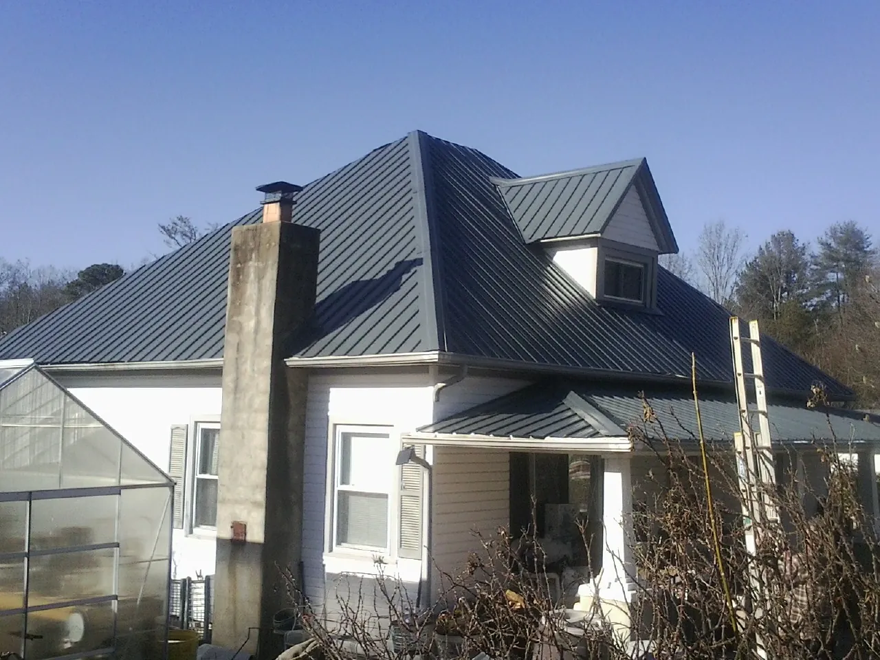 Dark blue standing seam metal roof on a white farmhouse with dormer — Slate & Tile Roof Repair by Roofing Brothers in Deanville