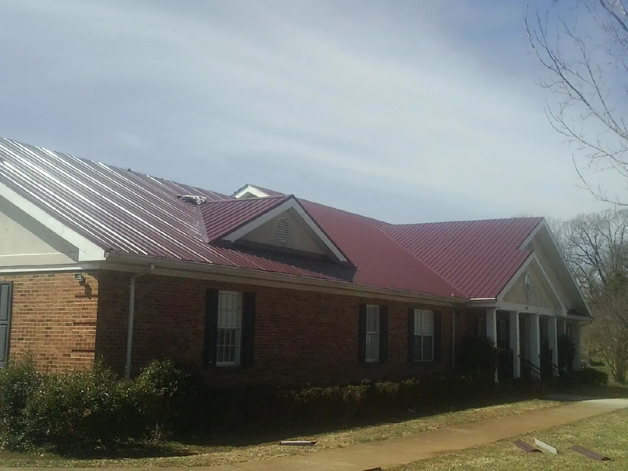 Red metal roof with gabled entries on a long brick building, from a Hail Damage Roof Repair job in Deanville