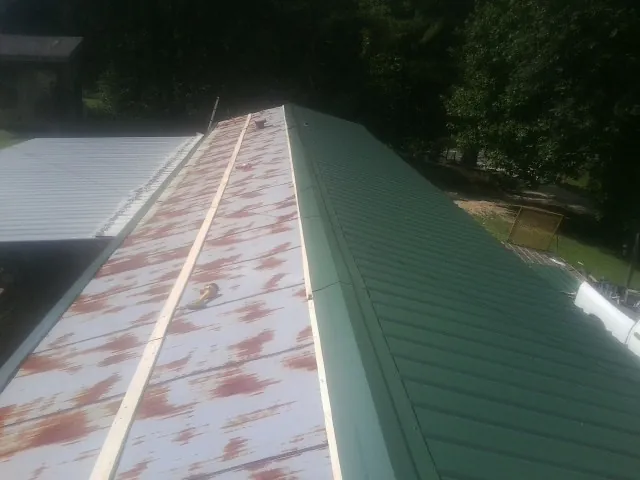 Old rusted panels beside newly installed green metal roofing — Wind Damage Roof Repair by Roofing Brothers in Deanville