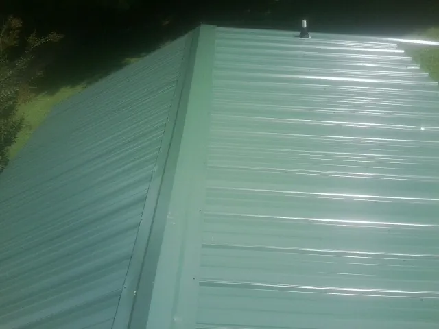 New green metal panels meeting at the ridge of a roof — Flat Roof Repair work by our crew in Deanville