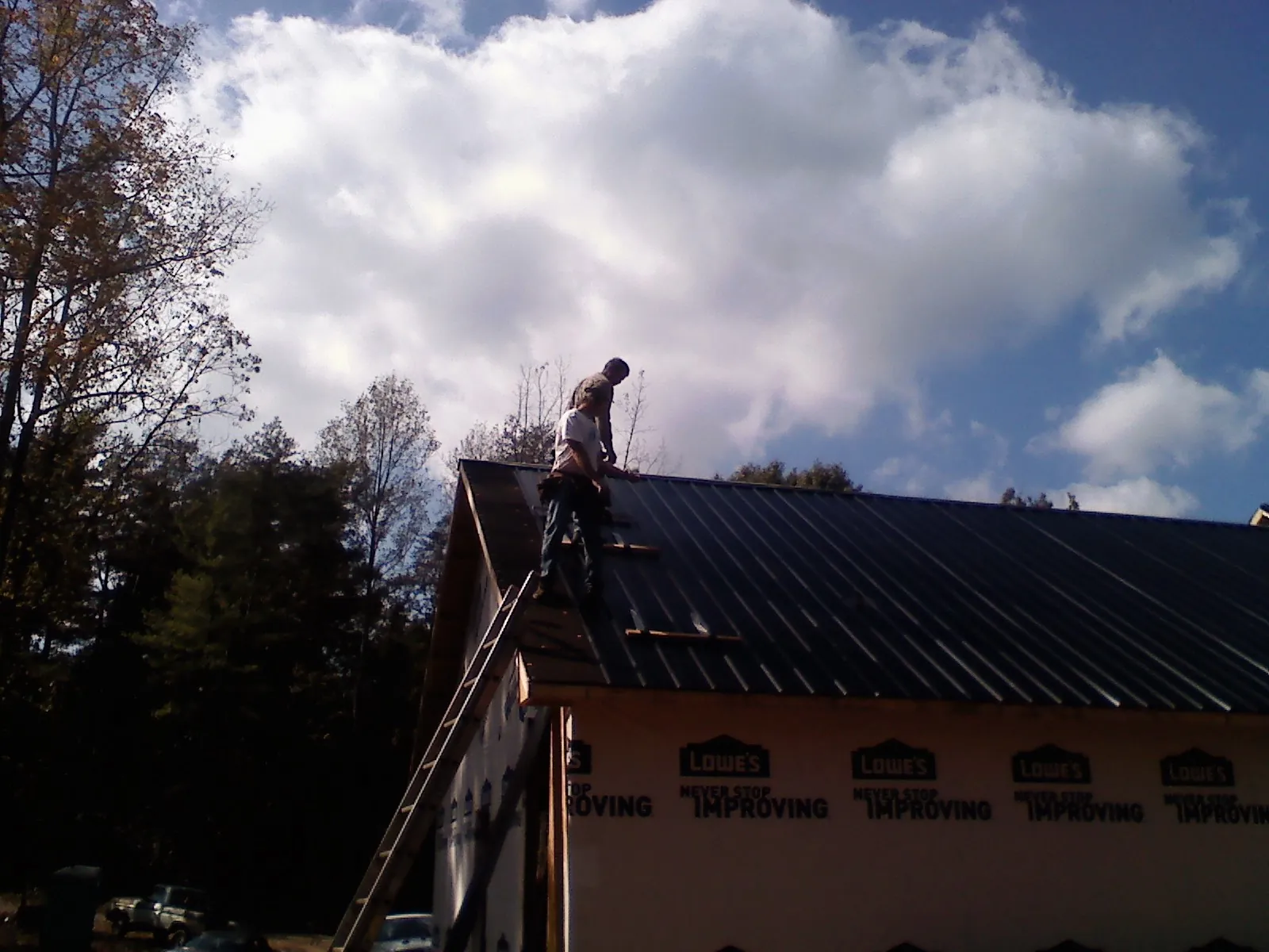 Roofer fastening dark metal panels high against a cloudy sky, from a Roof Inspection job in Deanville