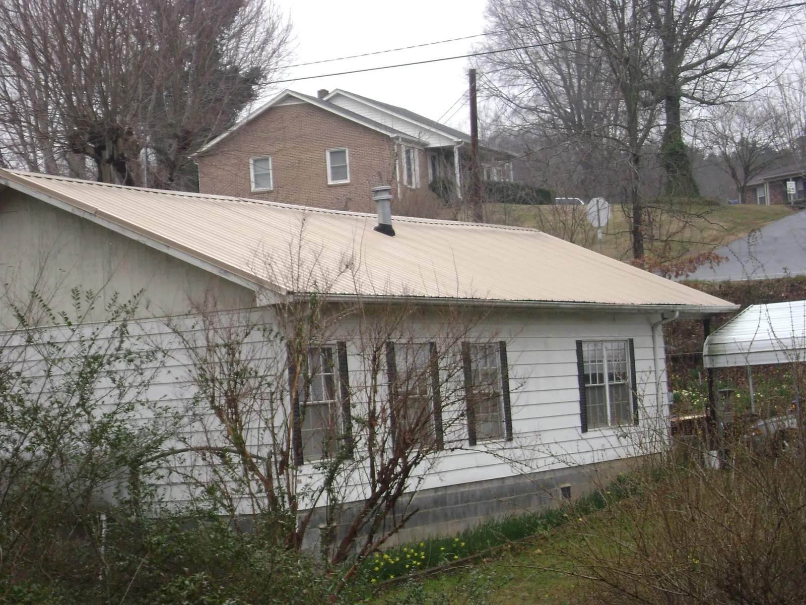 Tan metal roof on a white sided house set into a hillside — Commercial Roofing by Roofing Brothers in Deanville