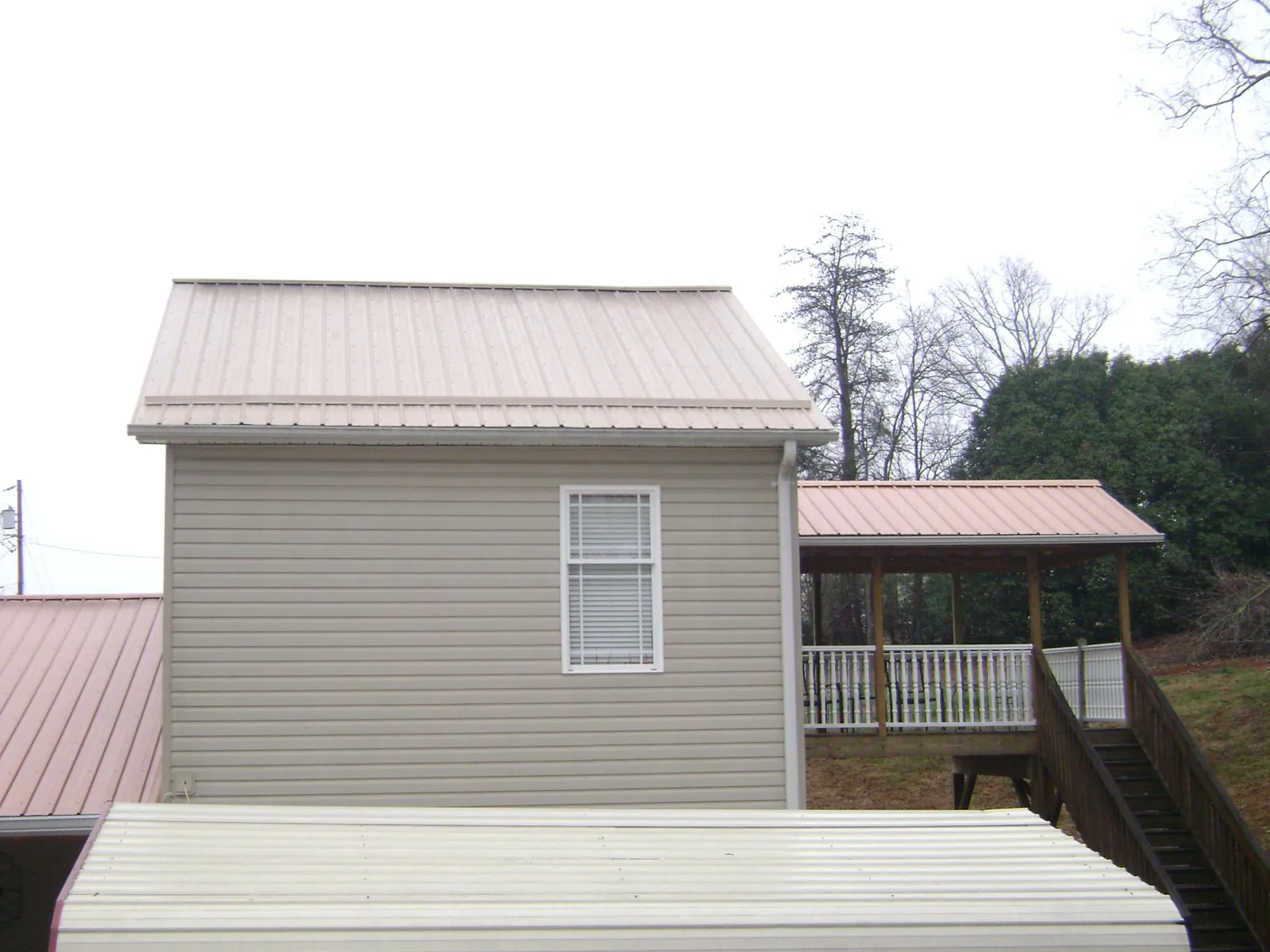 Tan metal roofs on a two story addition and attached porch, from a Roof Replacement job in Deanville